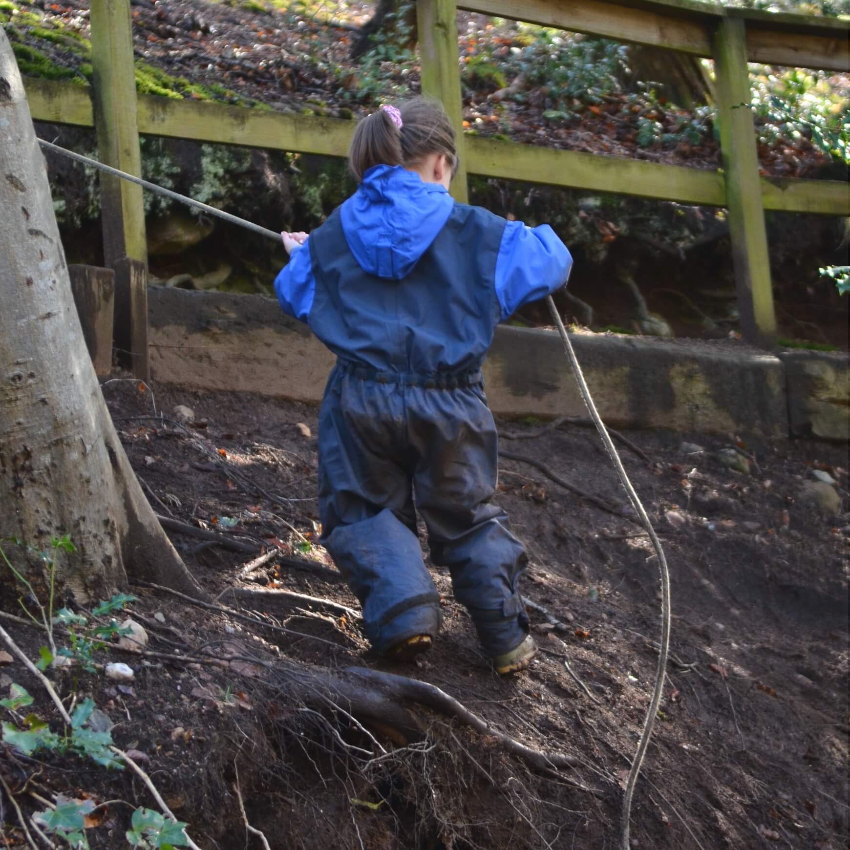 Child climbing a steep, muddy hill with a rope at Nature Nurture