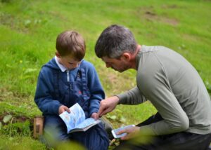 Child and adult reading from a book outside