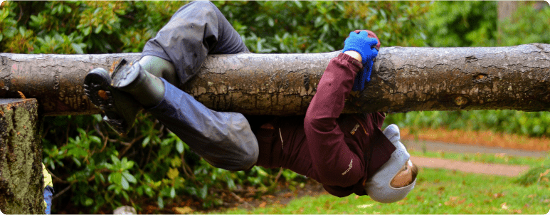 Child hangs from a suspended log on the play ground