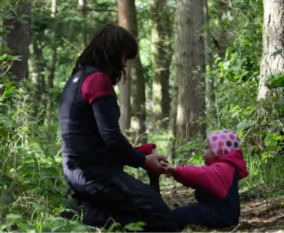 Adult and child sit face to face in the woods