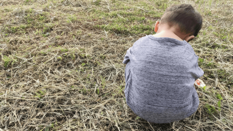transitions child sitting on the grass with head bent looking sad