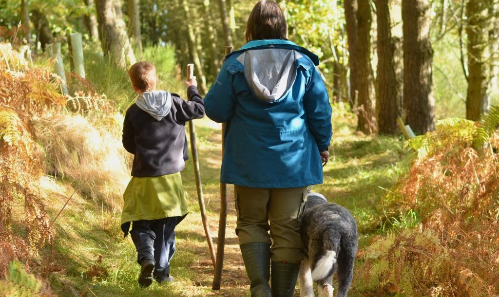 Nature Nurture in Practice - Child, adult and dog walk along a woodland path in the sunshine