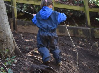 Child climbing a steep, muddy hill with a rope at Nature Nurture